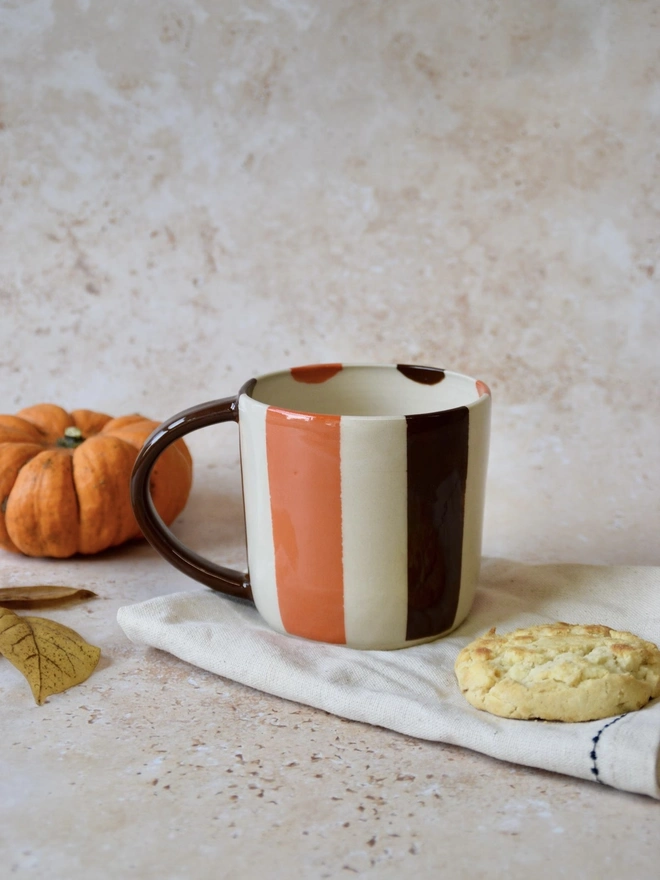 Bonbon Mug — handmade ceramic striped mug in brown and orange, styled with biscuit and pumpkin