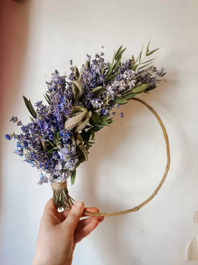 Lavender, Sage, Delphiumn & Eucalyptus Wreath seen held by. a hand.