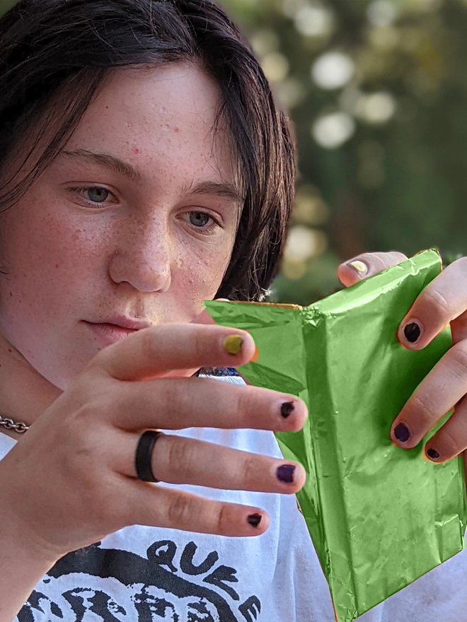 Happy young teenager opening green foil wrapped charity ruby chocolate bar