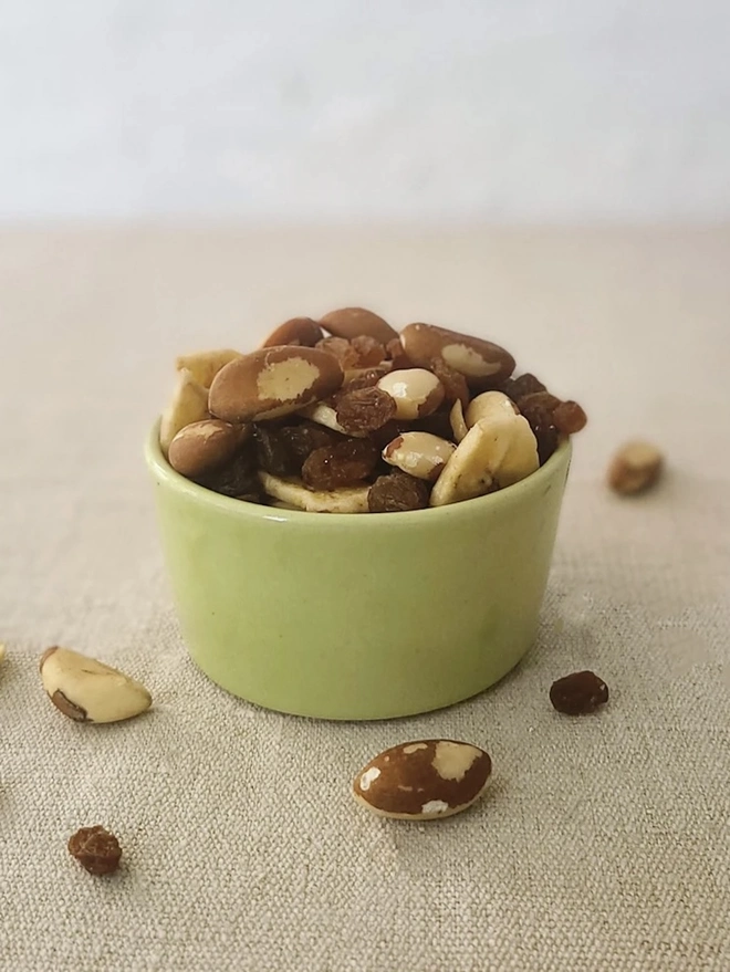 Classic Side Bowl, a colourful ceramic bowl on a wooden surface against a grey backdrop. It is accompanied by some nuts. 