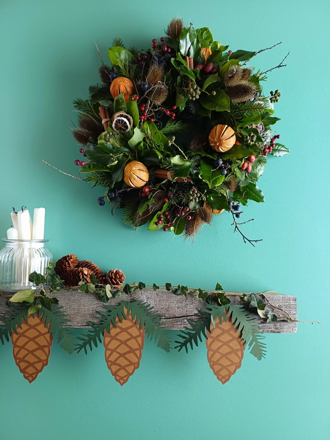 Pinecone Christmas Decoration displayed on wooden mantelpiece under papercut wreath