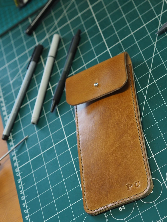 Personalised leather pencil sleeve. A tall slim hand dyed leather pencil case, handmade and hand stitched with golden brown thread. Personalised in the bottom corner with initials.