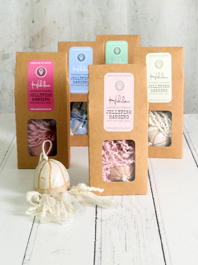 ceramic jellyfish decoration is sat on white washed floorboards in front of 5 boxes of jellyfish in blue, fushcia, pink, green and white 