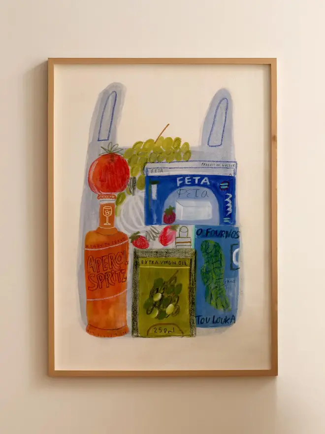 holiday shopping essentials print. illustrated print depicting traditional mediterranean groceries, such as aperol, olive oil, feta, tomatoes and grapes. print shown framed against a cream wall.