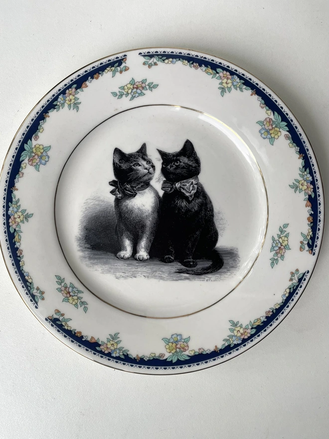 a vintage plate with an ornate border, in the centre of the plate is a vintage style black and white illustration of a black witch's cat