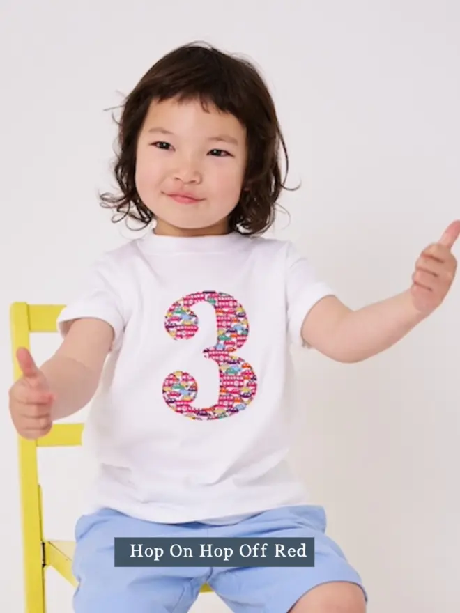 a 3 year old boy wearing a white birthday t-shirt with a number 3 cut from liberty cars and London buses print on the front
