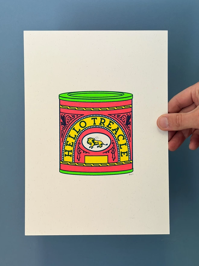 photograph of a hand holding an A4 screen print that shows the icon treacle tin design in flouro colours. The words Hello Treacle have been incorporated into the label design on the tin. Hello Treacle is Cockney rhyming slang for along with 'treacle tart' that means swearheart