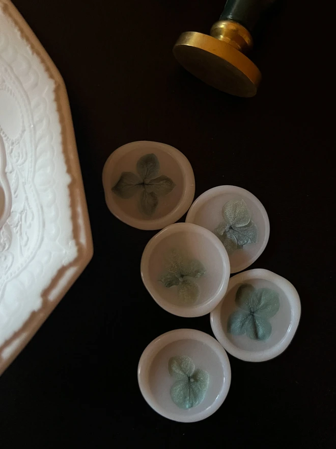 Vellum white wax seals with blue petals, wax seal stamp tool and ceramic trinket tray on black desk