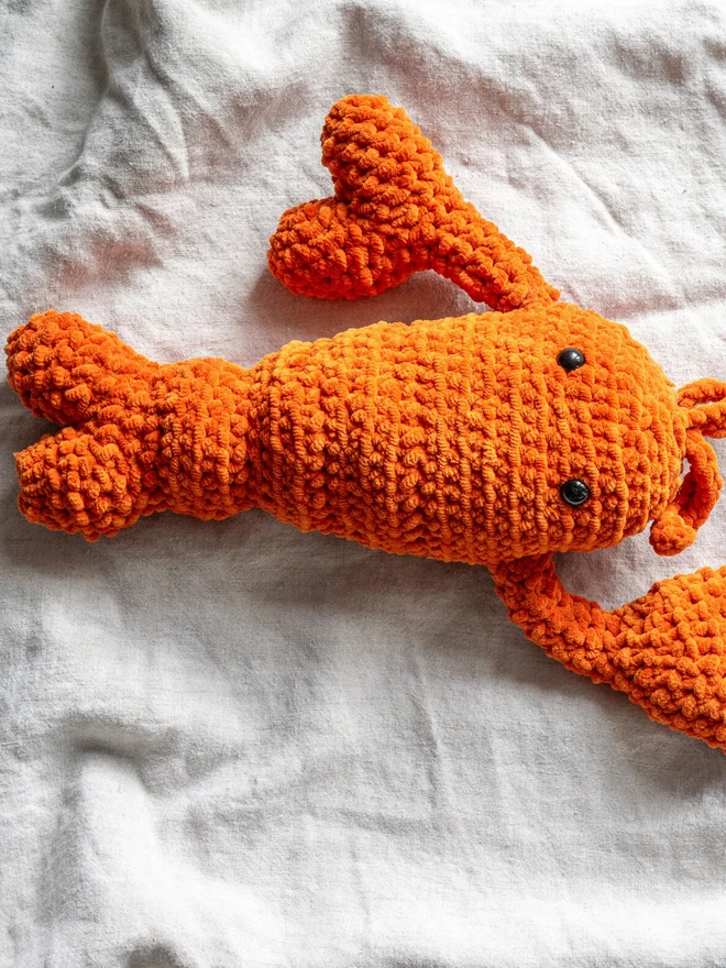 Chunky Chenille Cuddly Crochet Crustacean Lobster Plush, an orange lobster plush sitting on a white table cloth. 