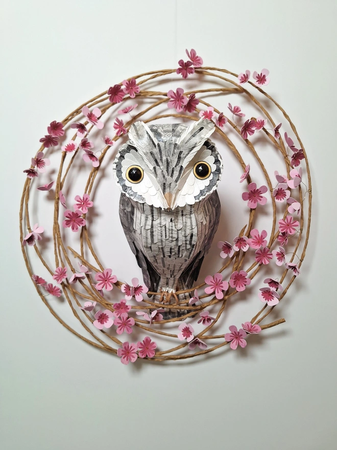 handmade wall art depicting a white faced owl, perched on a spring wreath of pink blooms