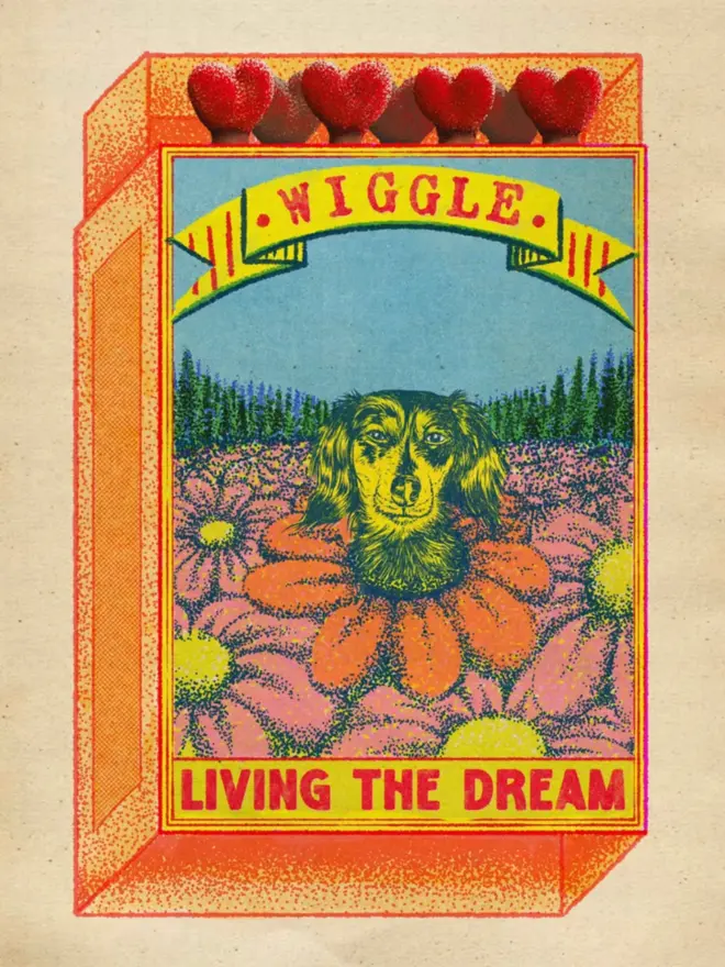 
An illustrated, retro-style matchbox features a long-haired dachshund. The dog's face is peeking out from the center of a large, daisy-like flower with pink and orange petals. The background is a field of more flowers with a line of trees and a bright blue sky. A banner at the top of the box reads "WIGGLE." The bottom of the box has a red-bordered section with the text "LIVING THE DREAM." The match tips on the side are heart-shaped, and the entire image has a grainy, textured appearance.