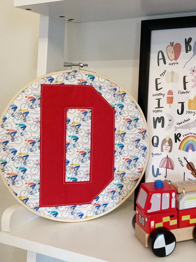 Personalised quilted hoop with a cyclist patterned fabric and the letter 'D' in red.