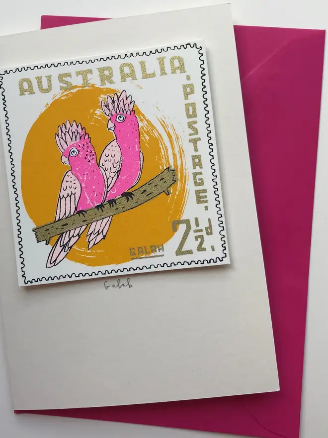 Bird Stamp Card Australian Galah, a white card with a colourful bird design on a red envelope above a white surface. 