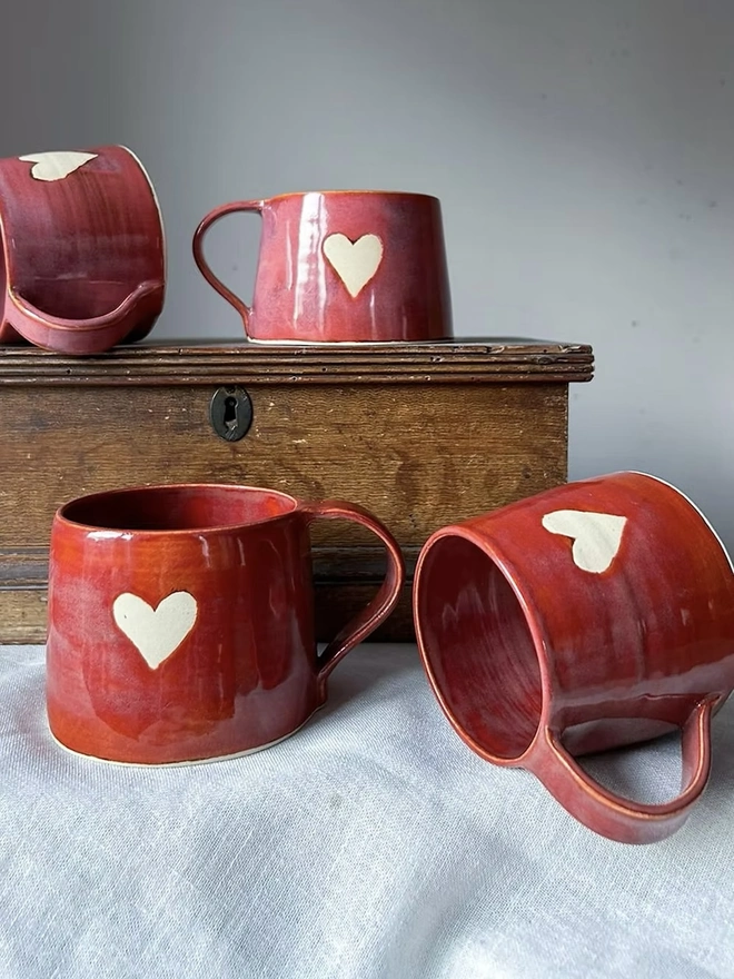 Heart Mug Cinnamon, a pair of heart mugs on a white surface in front of another pair of heart mugs on a wooden surface. 