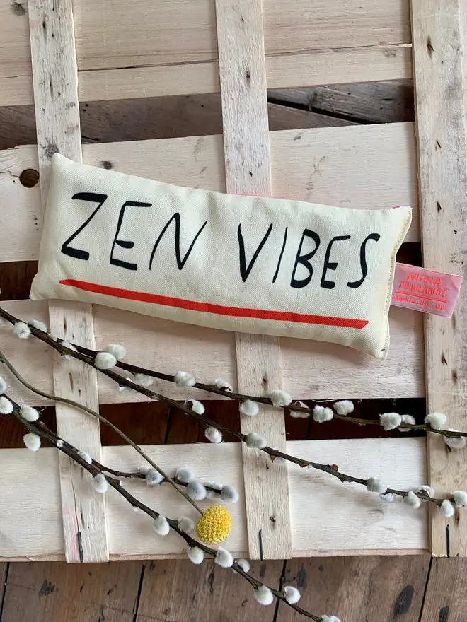 Lavender eye pillow with 'ZEN VIBES' in handwritten font, laid on wooden pallet