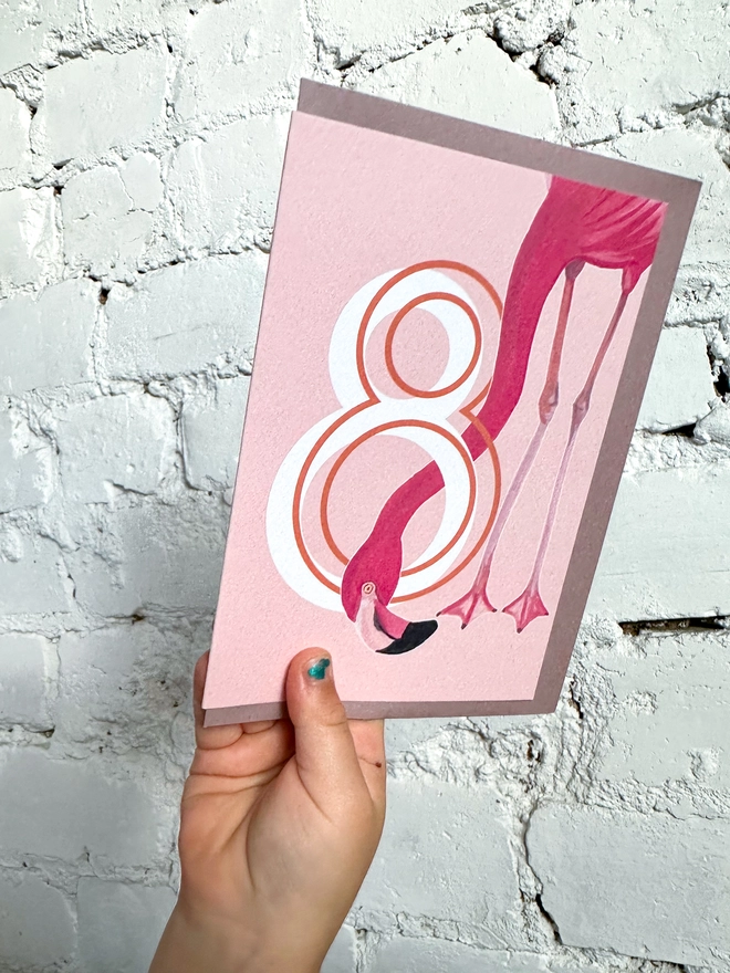 a pink card with a big white number 8 and an illustrated flamingo with a purple envelope
