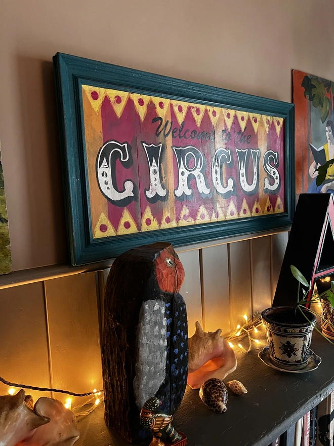 welcome to the circus sign, with colourful stripes of pink, yellow and orange with a teal frame and zig zag pattern at the top and the bottom. surrounded by a teal frame