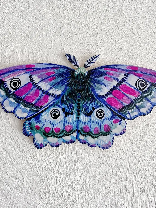 wooden emperor moth wall decoration. blue wooden moth hung on plain white wall.