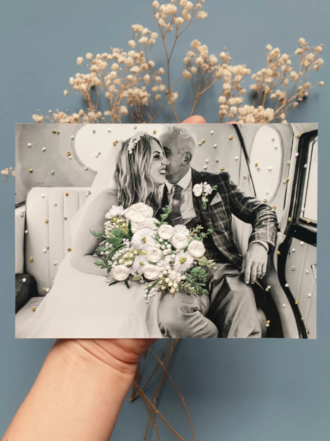 Embroidered wedding photo,embroidered bouquet and confetti on B&W photo, held over blue background