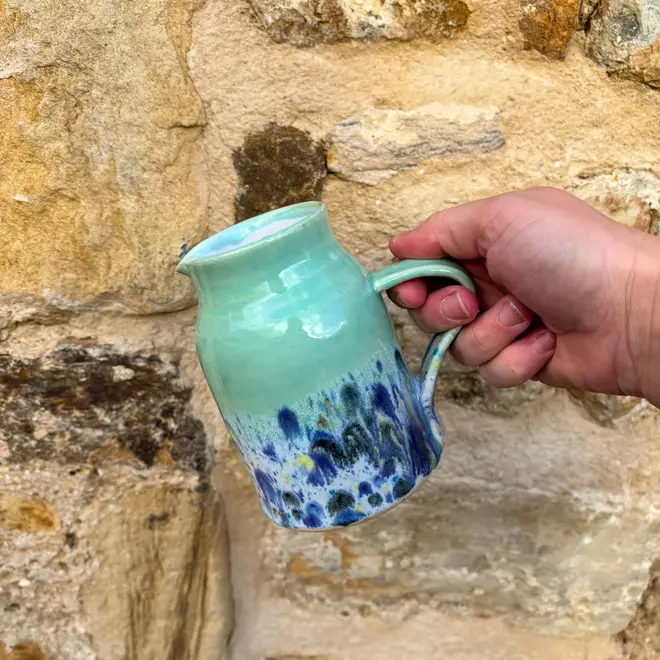Shoreline Medium Jug, a colourful jug being poured against a brick wall backdrop. 