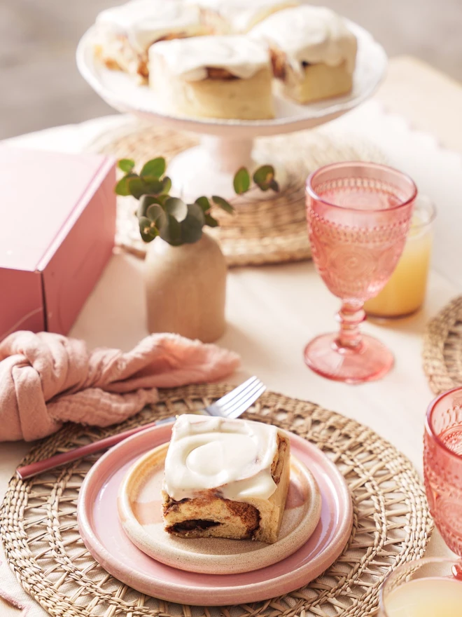 Cinnamon bun on a brunch table with a cake stand with cinnamon buns in the background