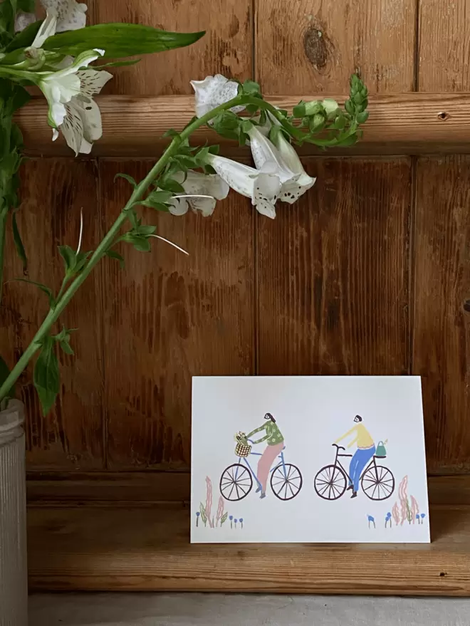 girl and boy on a bike greetings card, with foxgloves surrounding the card.