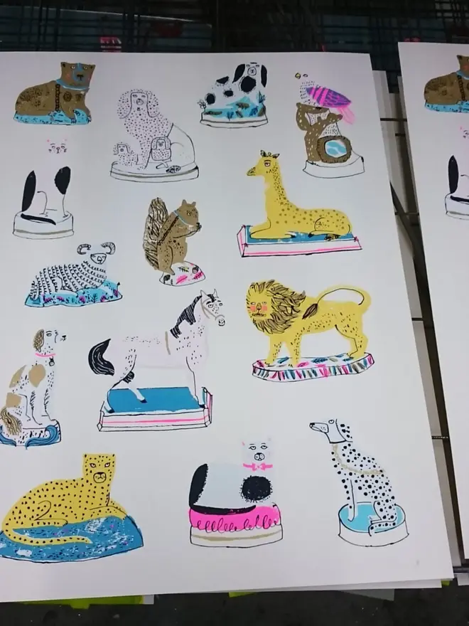 Pottery Animals Screenprint Paws And Claws (& Eight Hooves), a collection of colourful animal designs on a white screenprint. It is stacked on a studio rack. 