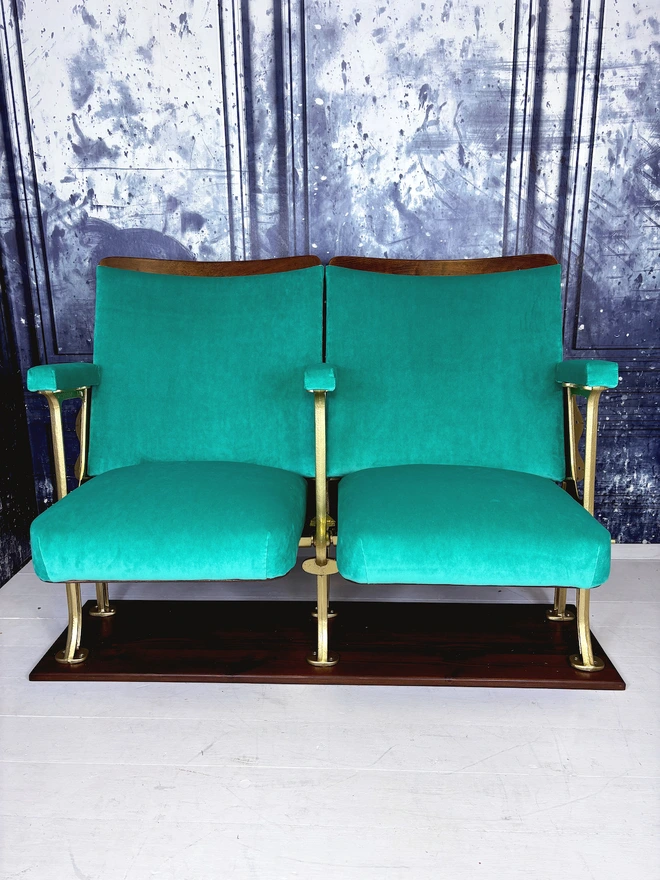 Set of two vintage refurbished cinema seat upholstered in a beautiful green plain velvet.  The cinema seats have gold legs and are mounted onto a wood plinth.  The flip down seats are open showing off their velvet upholstery