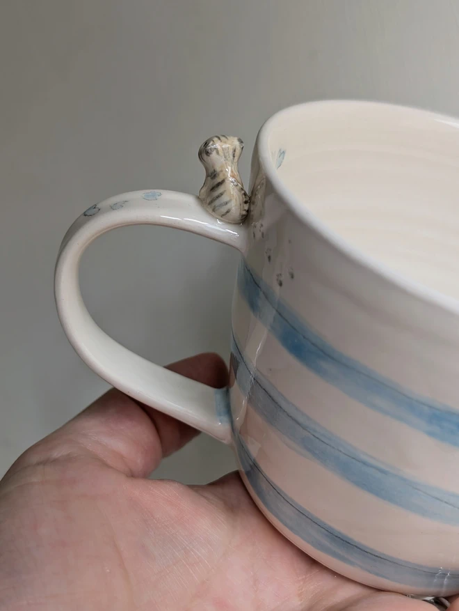 pottery cup with blue stripes and a tiny ceramic cat on the handle