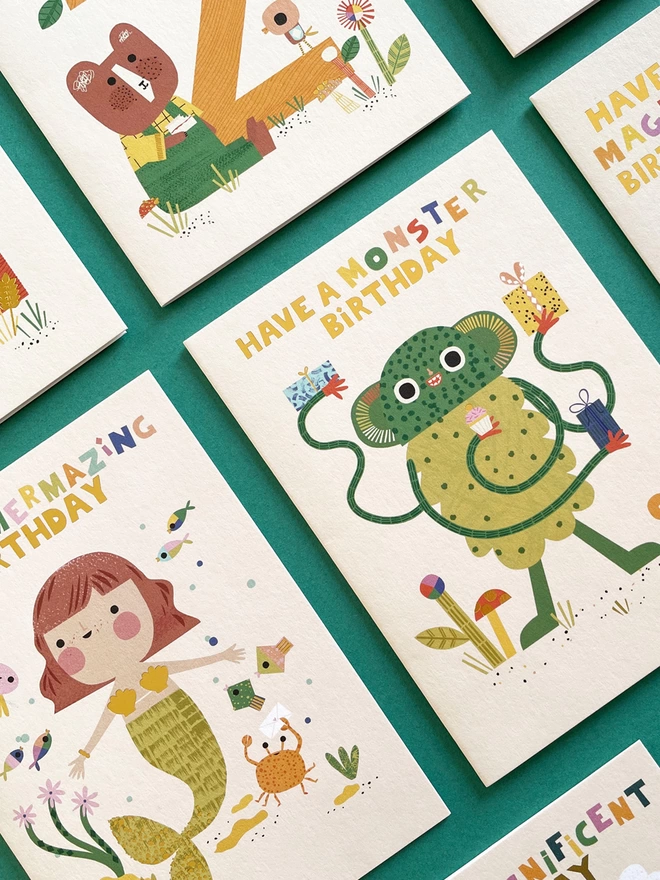 A flatlay of joyful children’s birthday cards featuring cute whimsical characters from bears to birds, mermaids and monsters. 