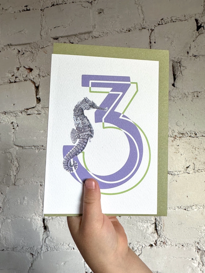 a white card with a big purple number 3 and an illustrated seahorse with a green envelope
