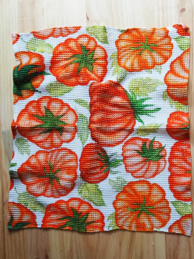 Tomato Waffle Tea towel, against a wooden table. 
