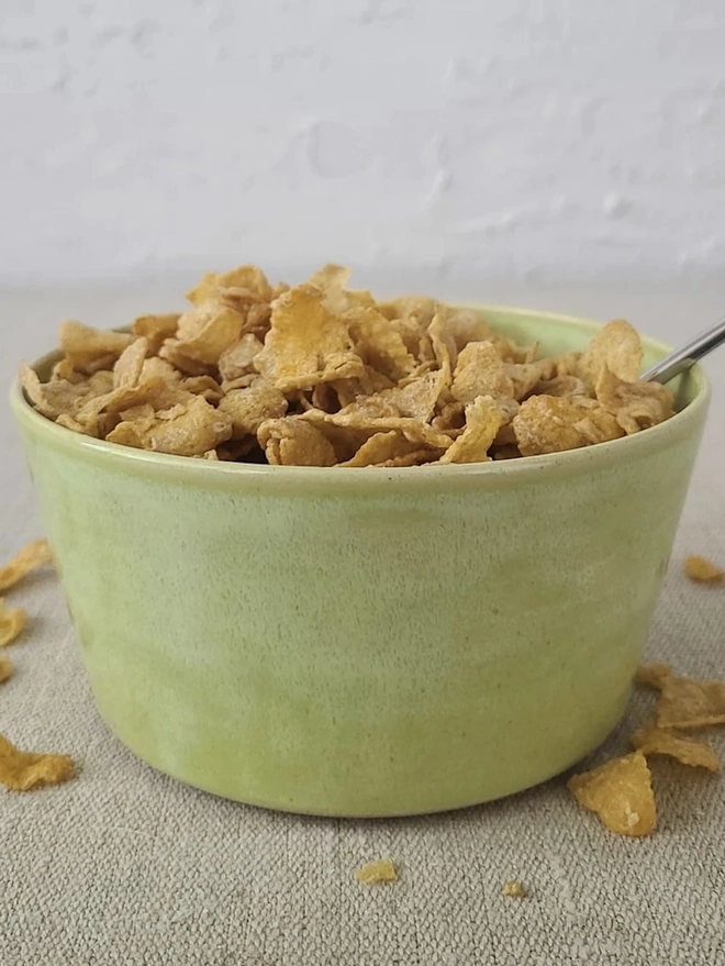 Classic Ceramic Breakfast Bowl, a breakfast bowl sitting on a grey carpet against a plain backdrop. It is accompanied by some cereal and a spoon. 