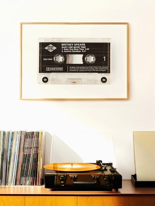 baby one more time britney spears cassette print. framed print hung on wall above record player and vinyl collection.