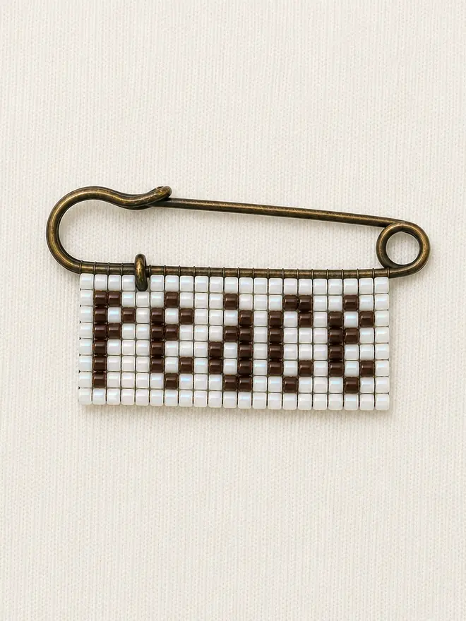 beaded 'peace' pin. a beaded pin badge with the word peace in brown lettering on a pearl background.