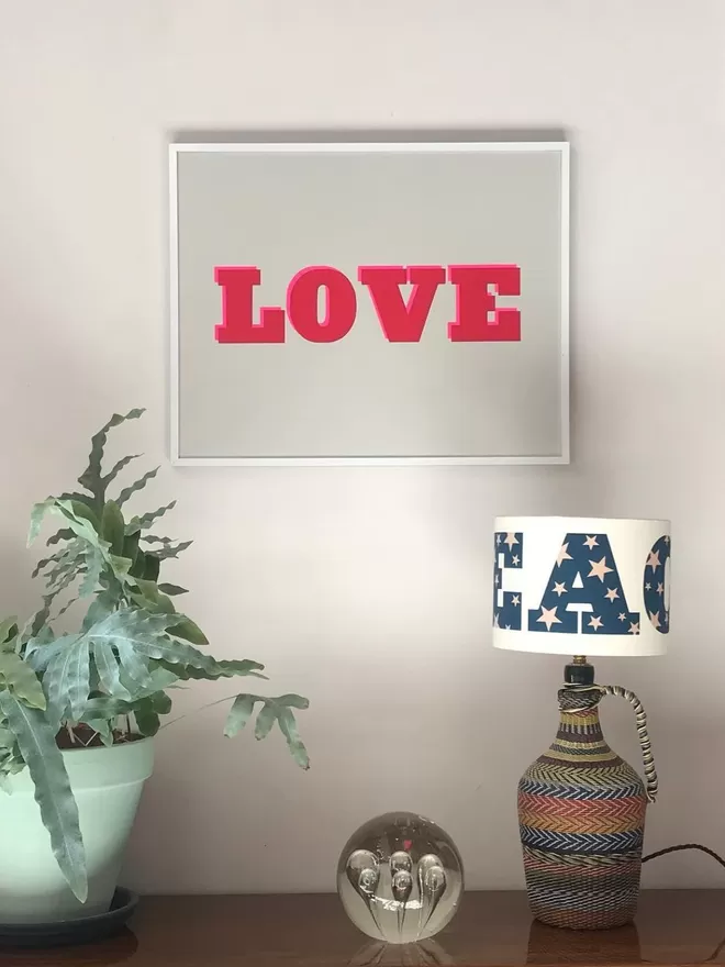 Love Screen print seen framed on a wall seen with a dandy star lamp.