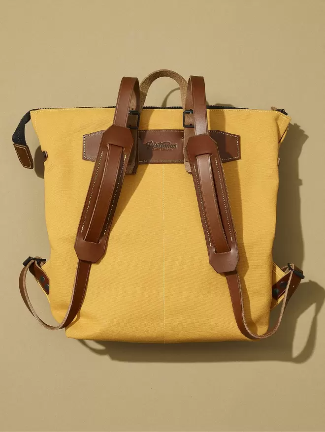 Back view of the yellow Shortwood zip top backpack with brown leather trim and black hardware.