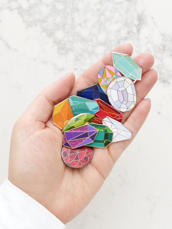Hand holding out birthstone enamel pin badges