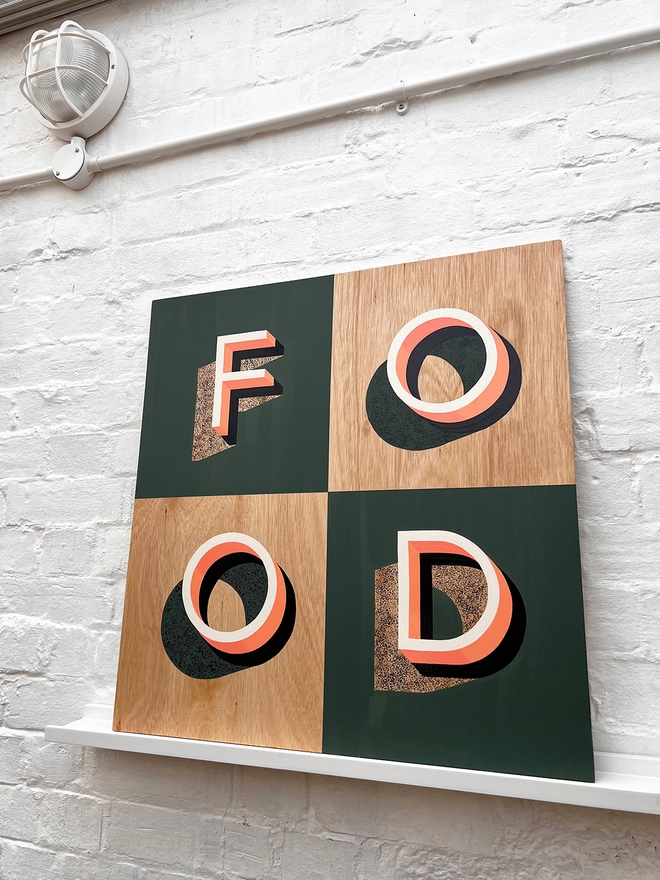 FOOD hand painted sign in coral, green and aubergine, against a white brick wall, at an angle. 