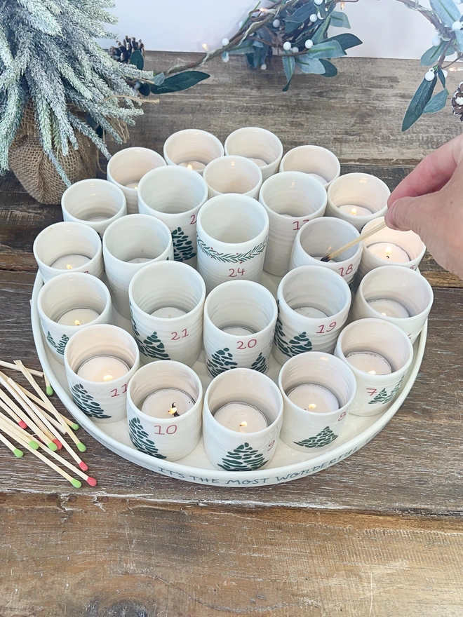 alternative advent tray with 24 numbered candle holders on a rustic table top with christmas tree and matches