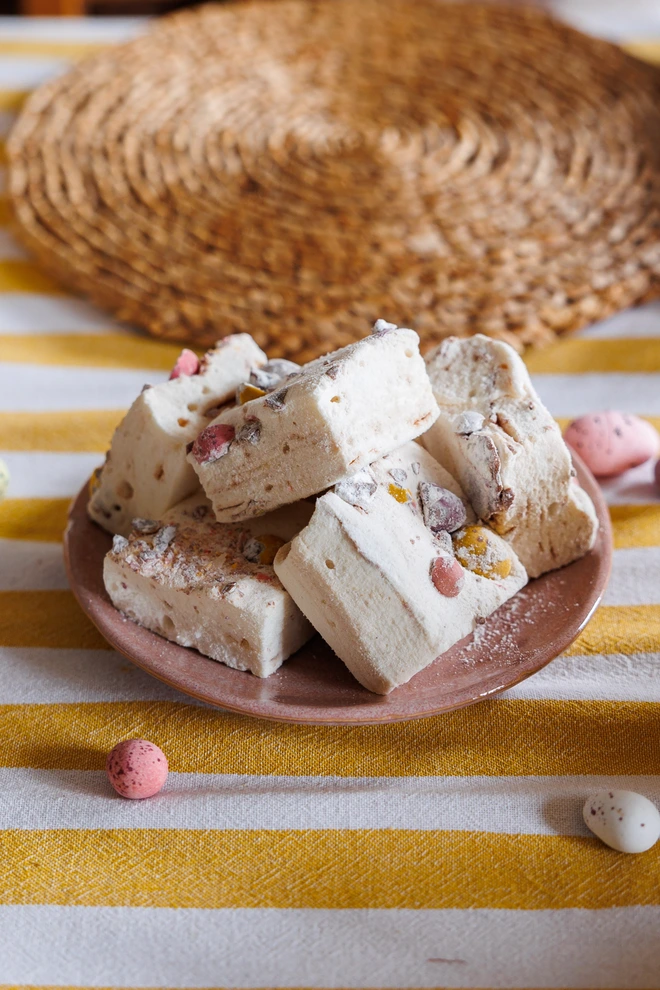 Mini Eggs Jumbo Marshmallows piled on top of a pink plate on a striped yellow tablecloth