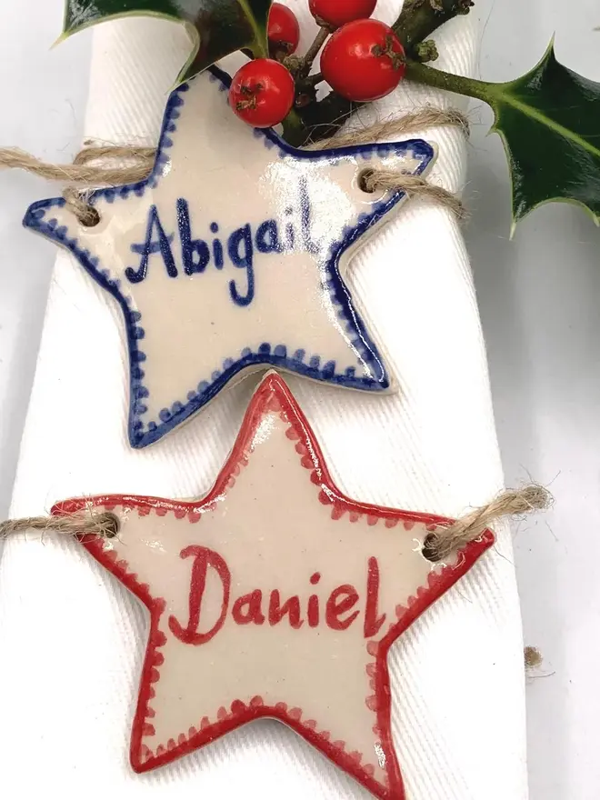 Personalised Ceramic Christmas Star Name Place Markers, a colourful ceramic start sitting on a white surface attached to a holly bush. 