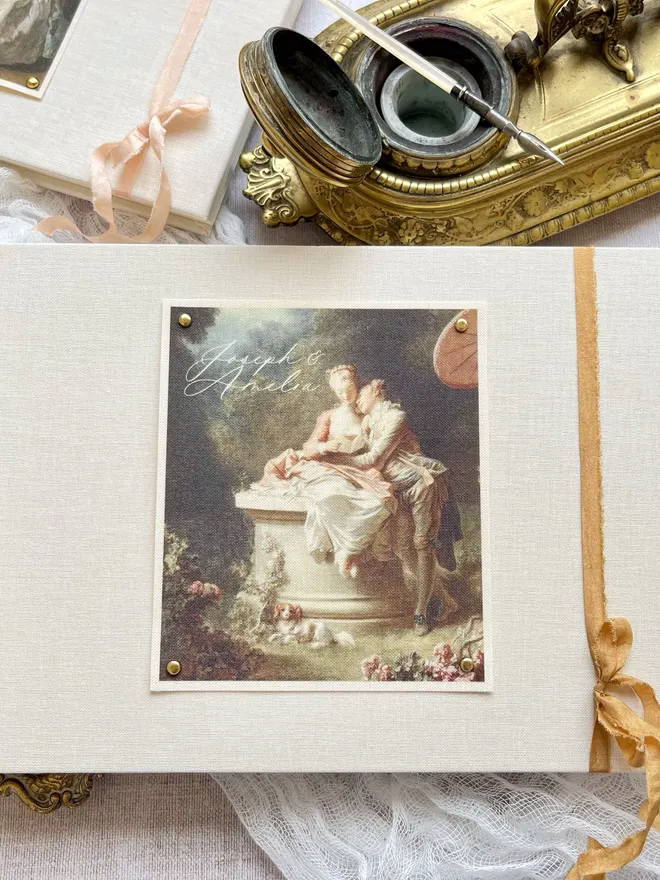 Luxury fabric printed wedding guest book featuring an images of lovers from an 18th century rococo work of art. Linen covered book finished with ribbon