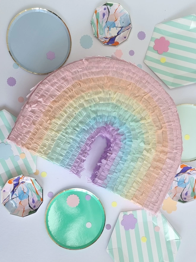 Rainbow pinata from pinyatay in pastel shades on a white background with paper plates and confetti