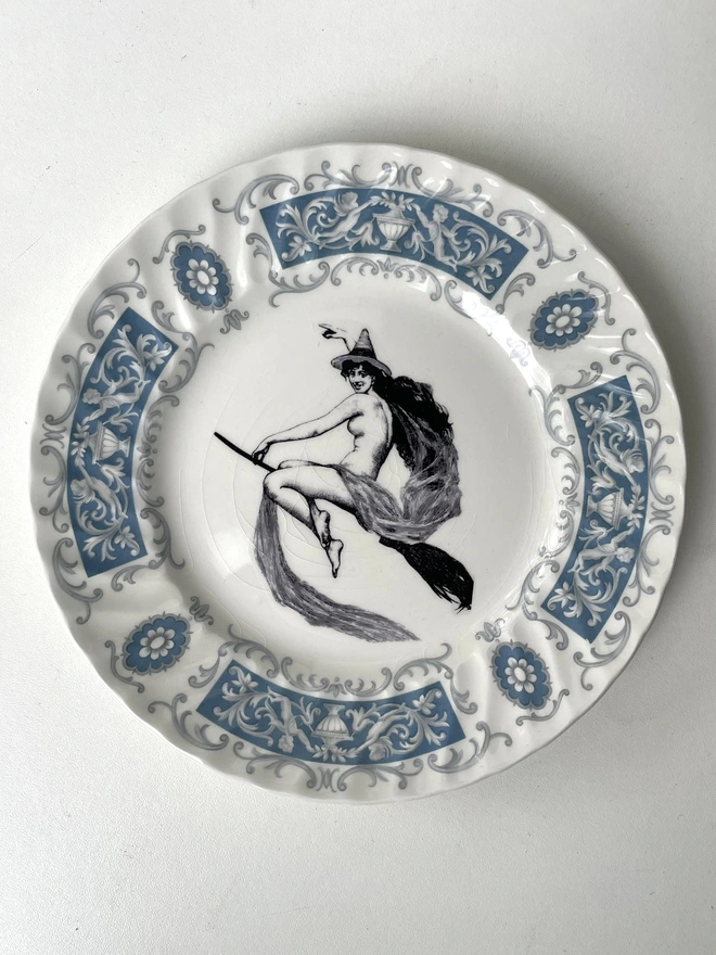 vintage plate with an ornate border, with a printed vintage illustration of a witch on a broomstick in the middle 