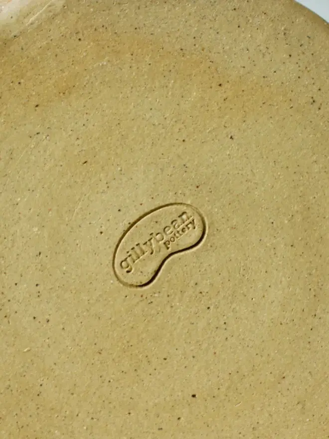 Bottom view of a ceramic mug showing the base and a stamped logo on the underside of the clay.