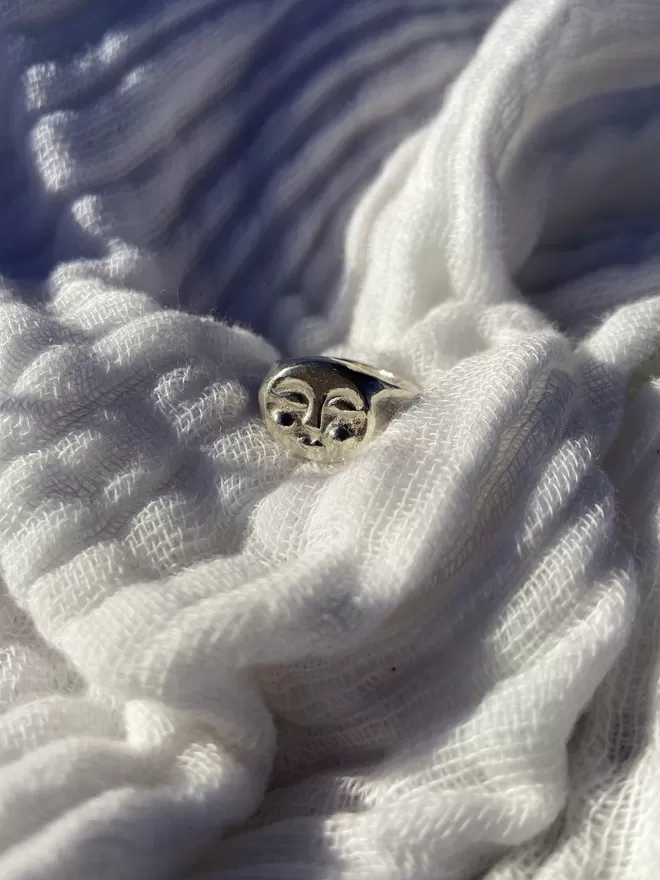 Image of silver hand carved moon face ring on white linen fabric 