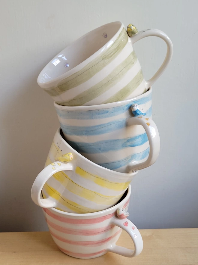 A stack of cups with yellow, pink, blue or green stripes with budgies on the handle