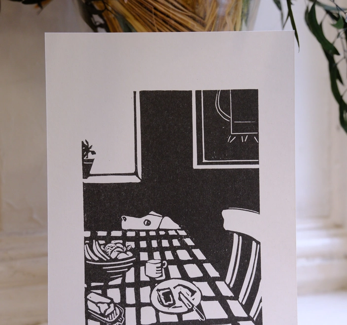 A black and white print shpwing a dog peering over a table at some toast