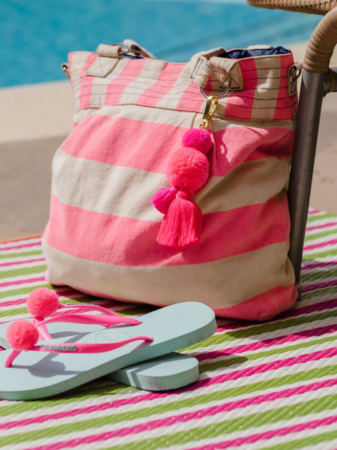 pom pom and tassel keyring. a pink tassel pom pom keyring photographed on a beach bag by a pool.